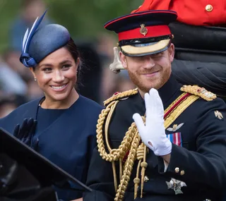 Prince Harry and Meghan Markle in formal attire, smiling and waving during a carriage procession.