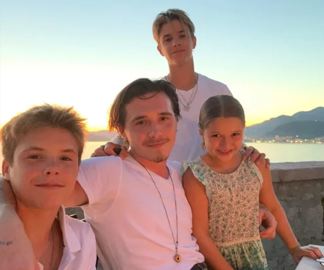Four people smiling, sitting together with a sunset and ocean in the background, enjoying a relaxed outdoor moment.