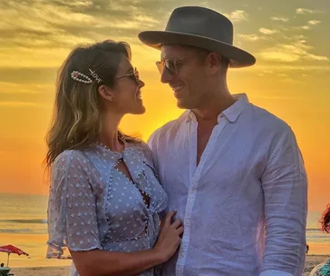 Man and woman smiling at each other during a beach sunset, both wearing sunglasses.