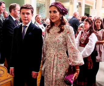 Crown Princess Mary in a Zimmerman dress at an event, standing beside a young boy, surrounded by elegantly dressed people.