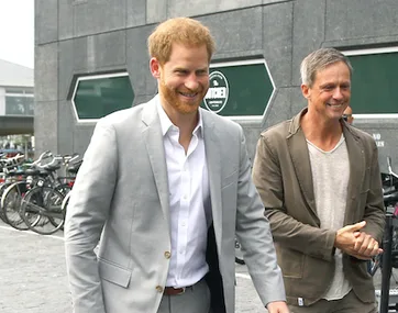 Two men walking and smiling outside a building with bicycles in the background.