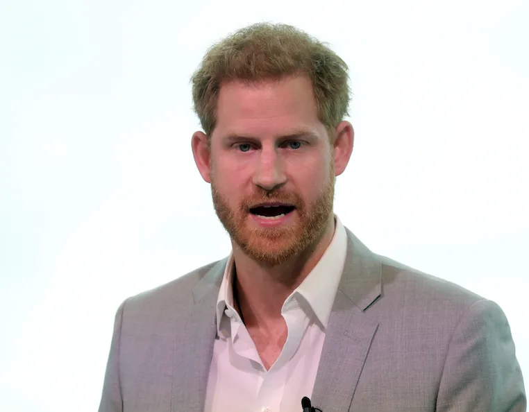 Man in a light grey blazer speaking, with a neutral background.