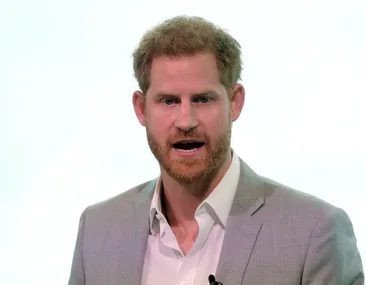 Man in a light grey blazer speaking, with a neutral background.
