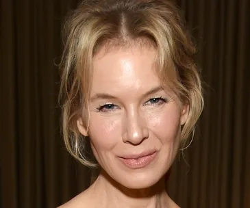 Portrait of a smiling woman with blond hair and soft lighting indoors.