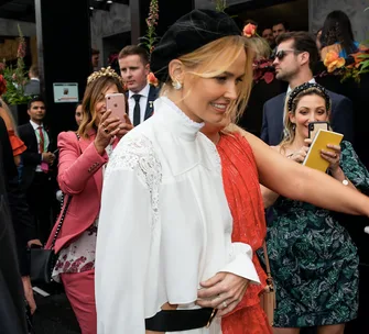 A woman in a white blouse and black cap surrounded by people, some using smartphones at an event.