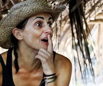 Woman in a straw hat with a surprised expression, sitting in a rustic setting.