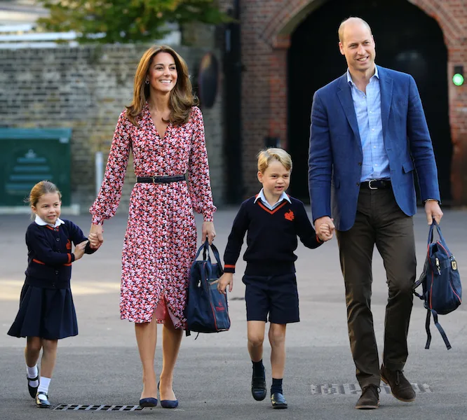 A family of four, dressed smartly, walking while holding hands. Adults carry school bags for children.