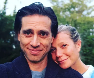 A couple smiling with greenery in the background, highlighting a close and joyful moment.
