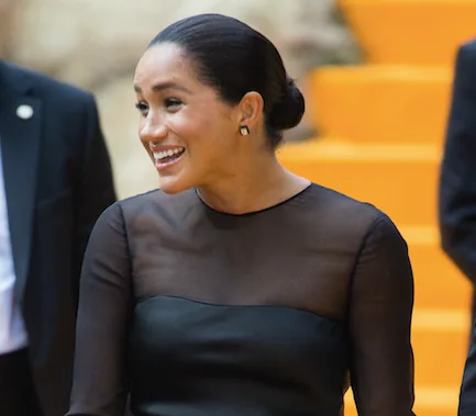 A woman in a black sheer dress smiling, with a blurred orange background.