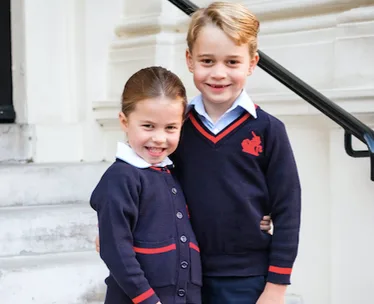 Two children in school uniforms smiling on steps.