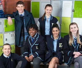 A group of six young people in school uniforms poses in front of lockers, smiling.