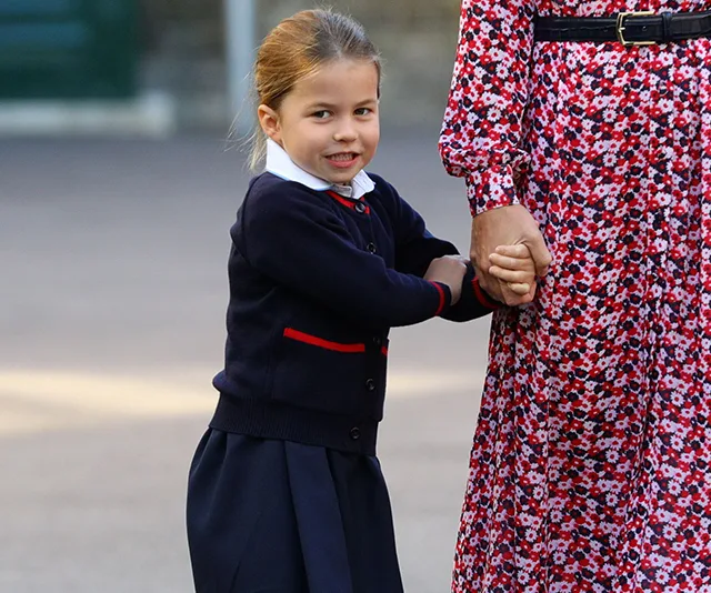 Young girl in school uniform holding hand of a person in a floral dress, smiling at the camera.
