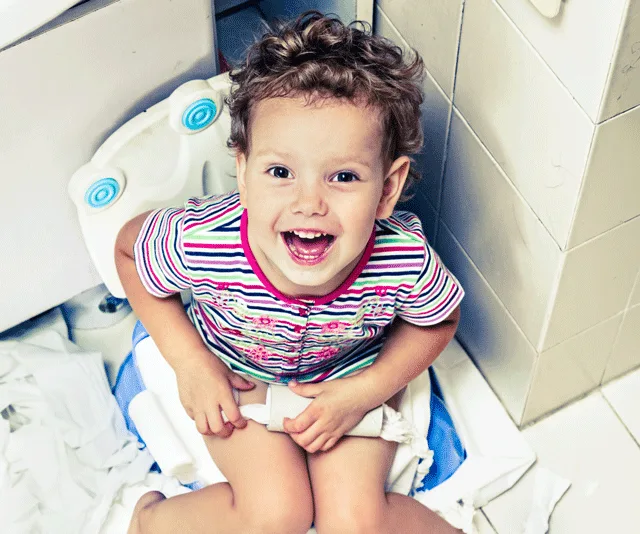 Toddler smiling on a potty chair, toilet paper scattered around.