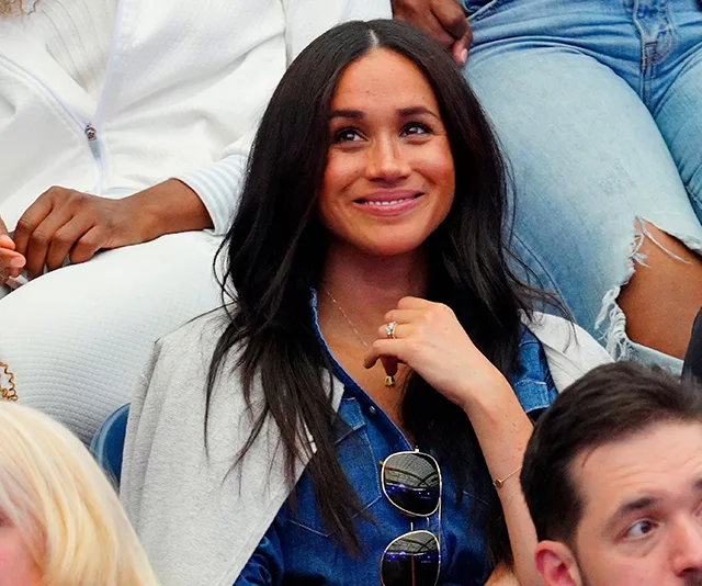 Meghan Markle smiling at the US Open, wearing a casual outfit and a necklace.