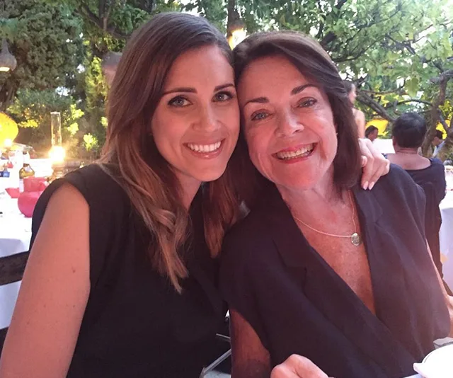 Two women smiling at an outdoor dinner setting, surrounded by trees and soft lighting.
