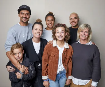 A diverse group of seven people smiling, including men, women, and children, against a plain background.