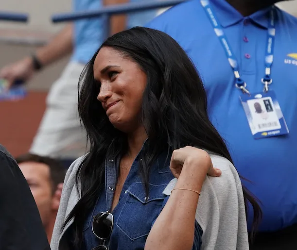 A woman with long dark hair in a denim shirt smiles at an event while standing beside a person in a blue uniform.