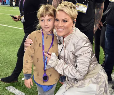 Singer Pink hugging her daughter Willow, at an event, both smiling. Willow wears a beige shirt with peace signs.