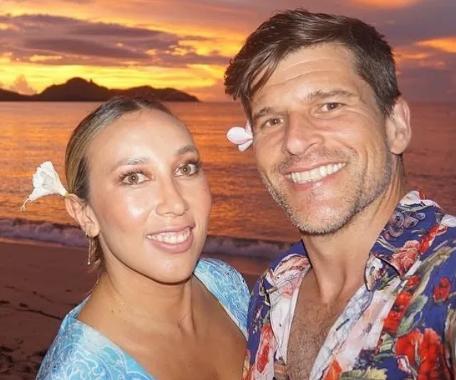Couple smiling on a beach at sunset with flowers in their hair.