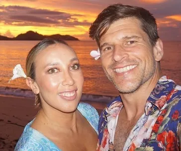 Couple smiling on a beach at sunset with flowers in their hair.