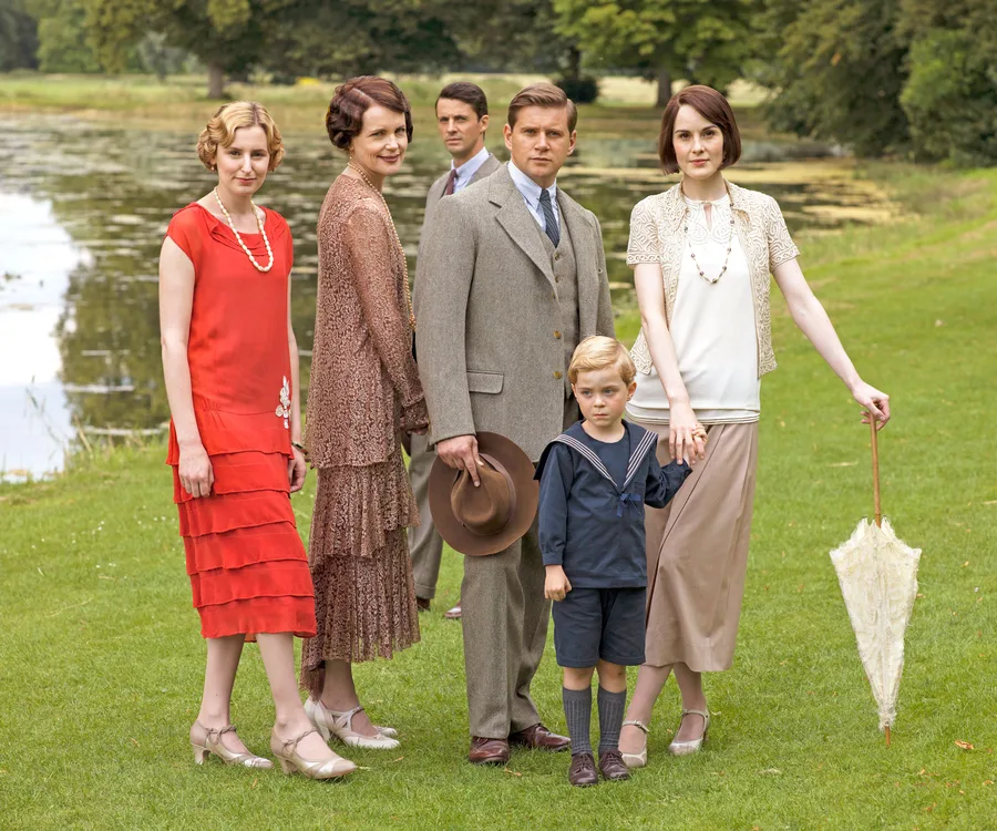Cast of "Downton Abbey" stand by a pond in 1920s attire.