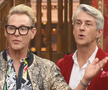 Two stylish individuals in a lively discussion; one in a patterned shirt and glasses, the other in a red jacket.