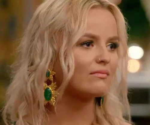 Blonde woman with large green earrings, wearing a nose ring, looking to the side.