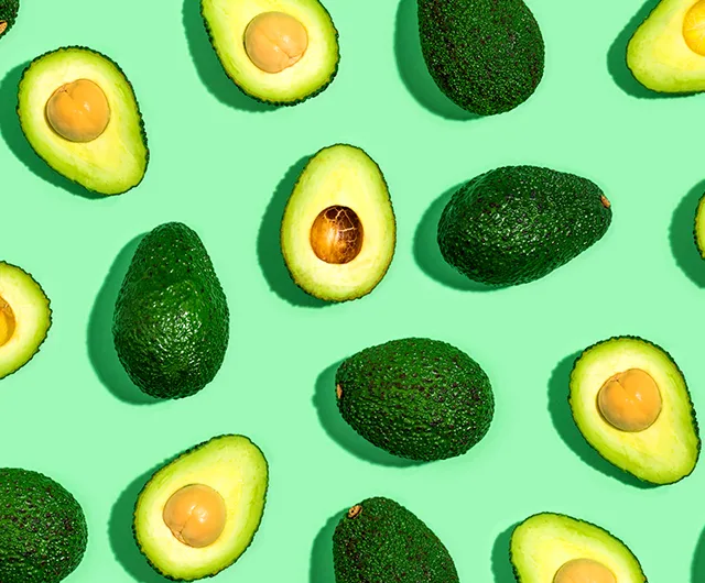 Avocados halved and whole arranged on a bright green background.