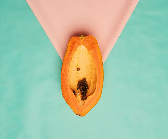 A halved papaya with seeds on a pink and teal background, symbolizing feminine themes.