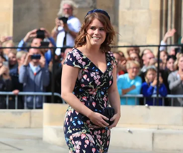 Princess Eugenie in a floral dress, smiling at a public event with a crowd in the background.