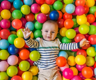 Baby in striped shirt smiling in a colorful ball pit.