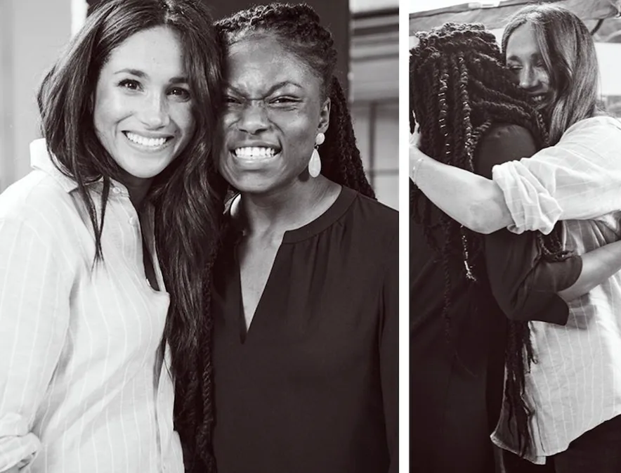 Two women smiling and embracing, one wearing a striped shirt, the other with braided hair and earrings, in a friendly moment.
