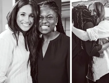Two women smiling and embracing, one wearing a striped shirt, the other with braided hair and earrings, in a friendly moment.