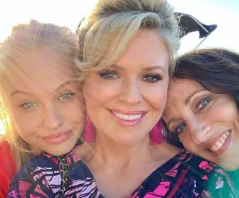 Three women smiling for a selfie, with the sun shining in the background.