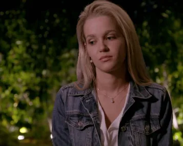 Helena in a denim jacket looks contemplative against a blurred greenery background.