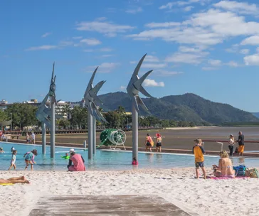 Children and adults enjoying the Lagoon Pool in Cairns with iconic metal fish sculptures and mountains in the background.