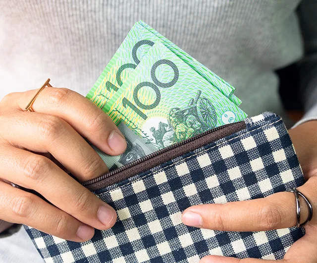 A person placing Australian 100-dollar bills into a black and white checkered wallet.