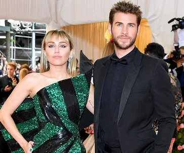 Two celebrities on a red carpet, one in a green and black dress, the other in a black suit, posing for photos.