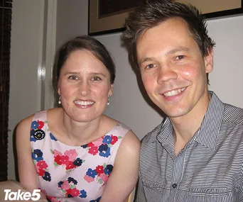 Couple smiling indoors, woman in floral dress, man in striped shirt, Take 5 magazine logo in corner.