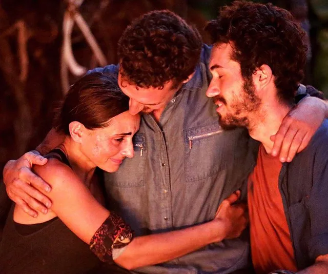 Three contestants from Survivor 2019 share an emotional group hug at the tribal council, showing solidarity and comfort.