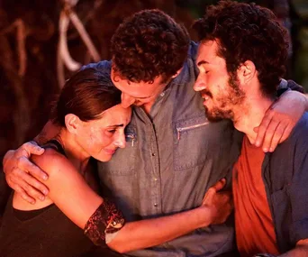 Three contestants from Survivor 2019 share an emotional group hug at the tribal council, showing solidarity and comfort.