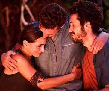Three contestants from Survivor 2019 share an emotional group hug at the tribal council, showing solidarity and comfort.