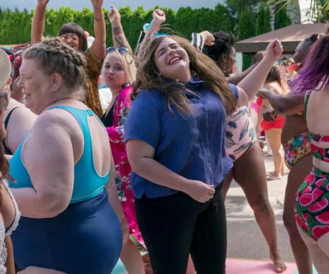 Group of people celebrating at a body-positive event, enjoying and dancing in colorful outfits outdoors.