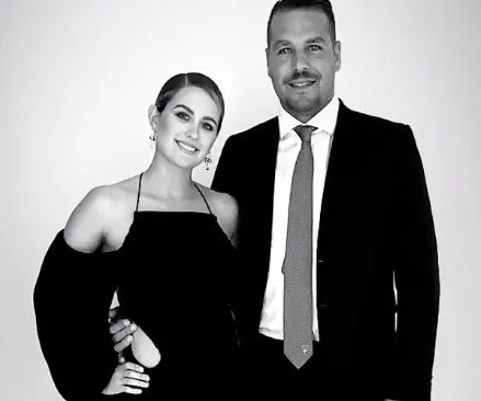 A couple dressed elegantly in black and white attire, smiling at the camera.