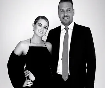 A couple dressed elegantly in black and white attire, smiling at the camera.