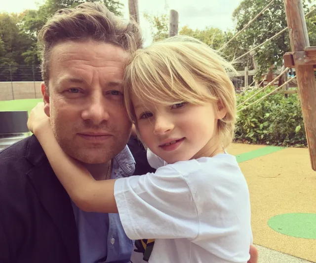 "Child hugging an adult outdoors, both smiling, with a green park setting in the background."