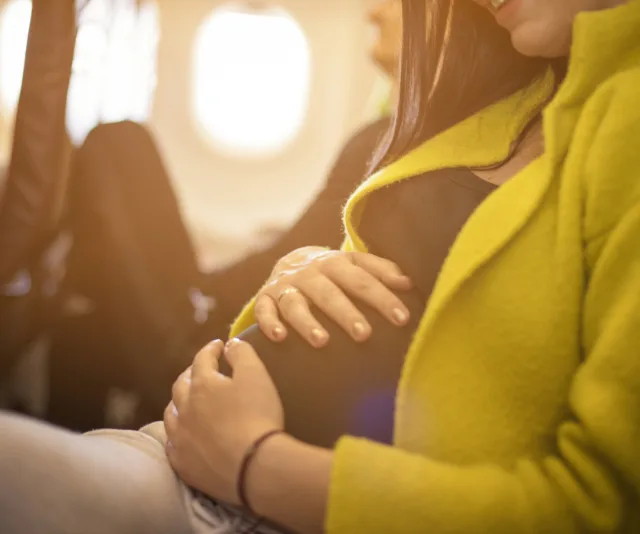 Pregnant woman seated in airplane, gently holding her belly.