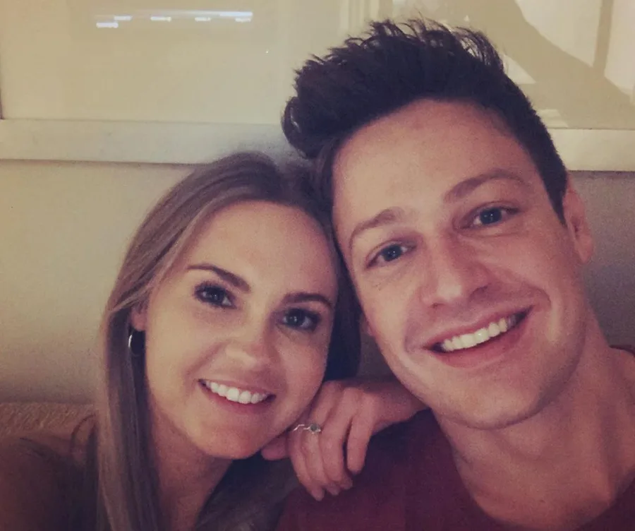 A couple smiling together, cheek to cheek, in a close-up selfie at home.