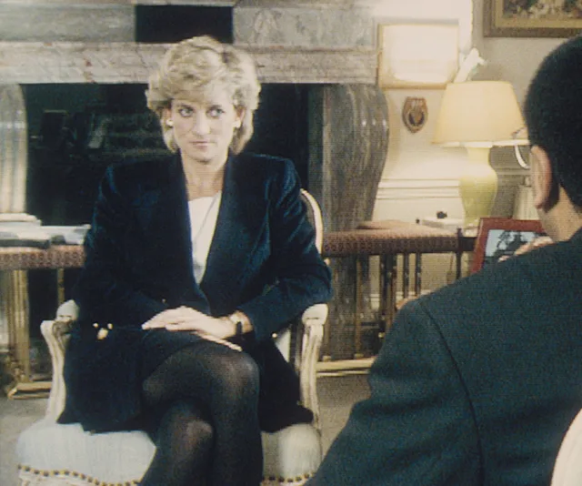 Princess Diana sits in an interview setting, facing an interviewer wearing glasses.