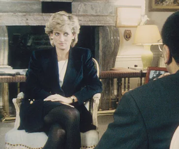 Princess Diana sits in an interview setting, facing an interviewer wearing glasses.